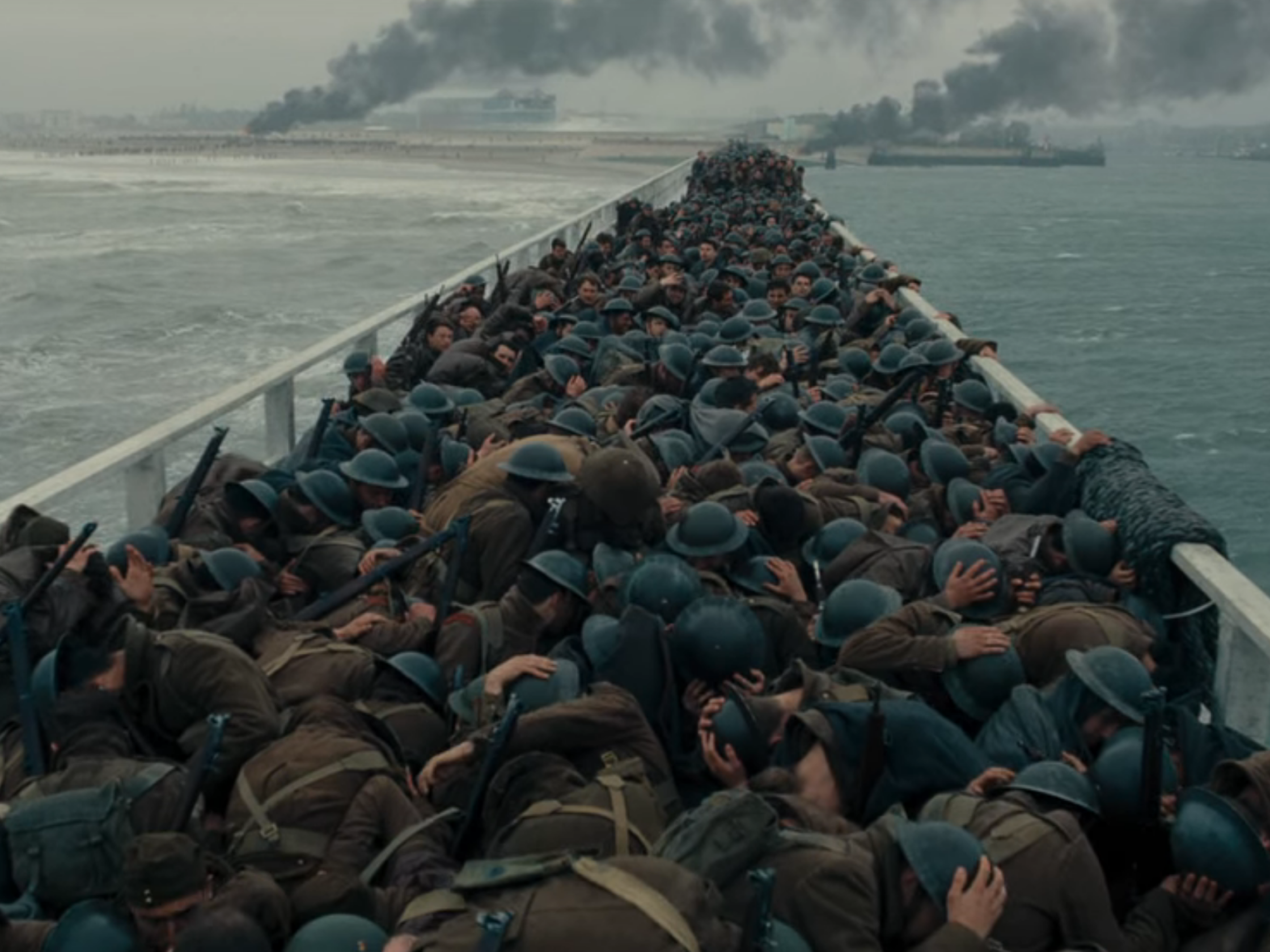 Ein Screenshot aus dem Film "Dunkirk" zeigt eine große Masse an Soldaten, die kaum von einander zu unterscheiden sind und sich auf einer Brücke vor einem Bombenangriff ducken