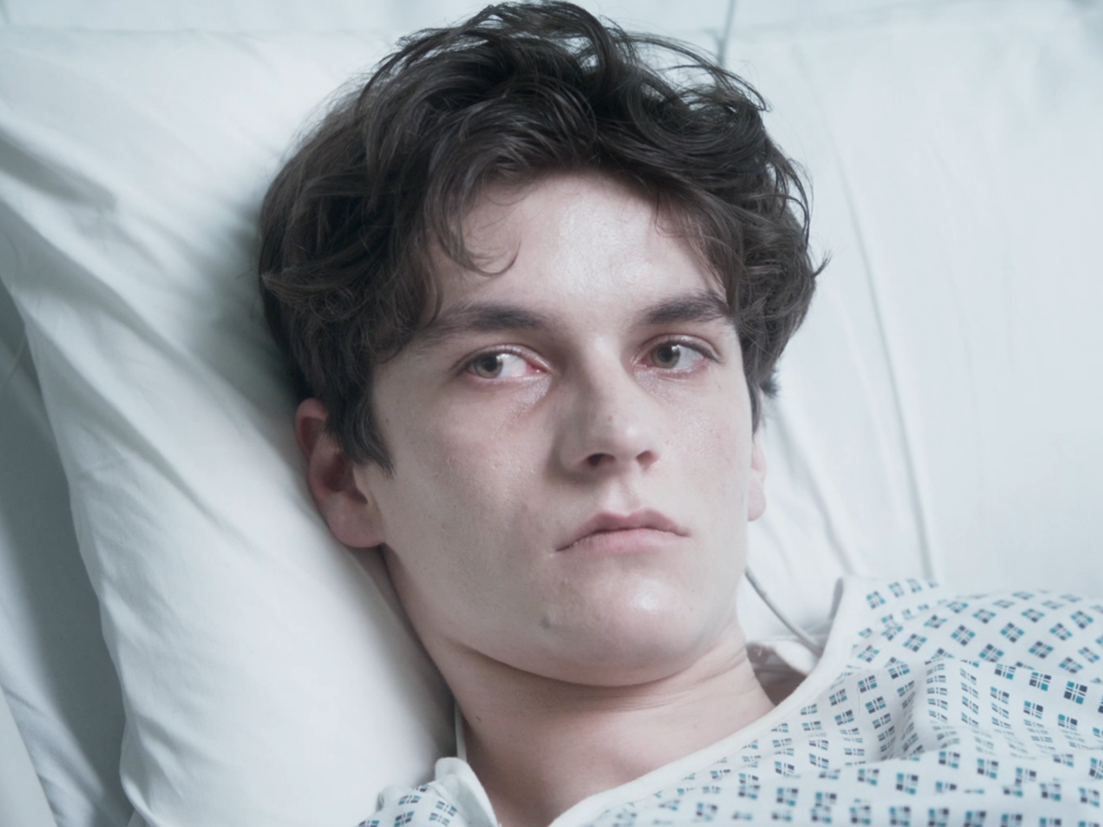 Das Bild zeigt die Hauptfigur Adam, ein Teenager. Er liegt in einem Krankenhausbett und trägt ein Krankenhausnachthemd. Man sieht nur sein Gesicht und seinen Hals. Seine dunkelbraunen Haare sind etwas länger und fallen locker in seine Stirn. Er hat grüne Augen, ein sehr blasses, krankes Gesicht und tiefe Augenringe. Trotz seiner scharfen Gesichtszüge wirkt er sehr jung, noch wie ein Kind. Er sieht sehr ernst und etwas traurig aus, als würde er über etwas nachdenken.