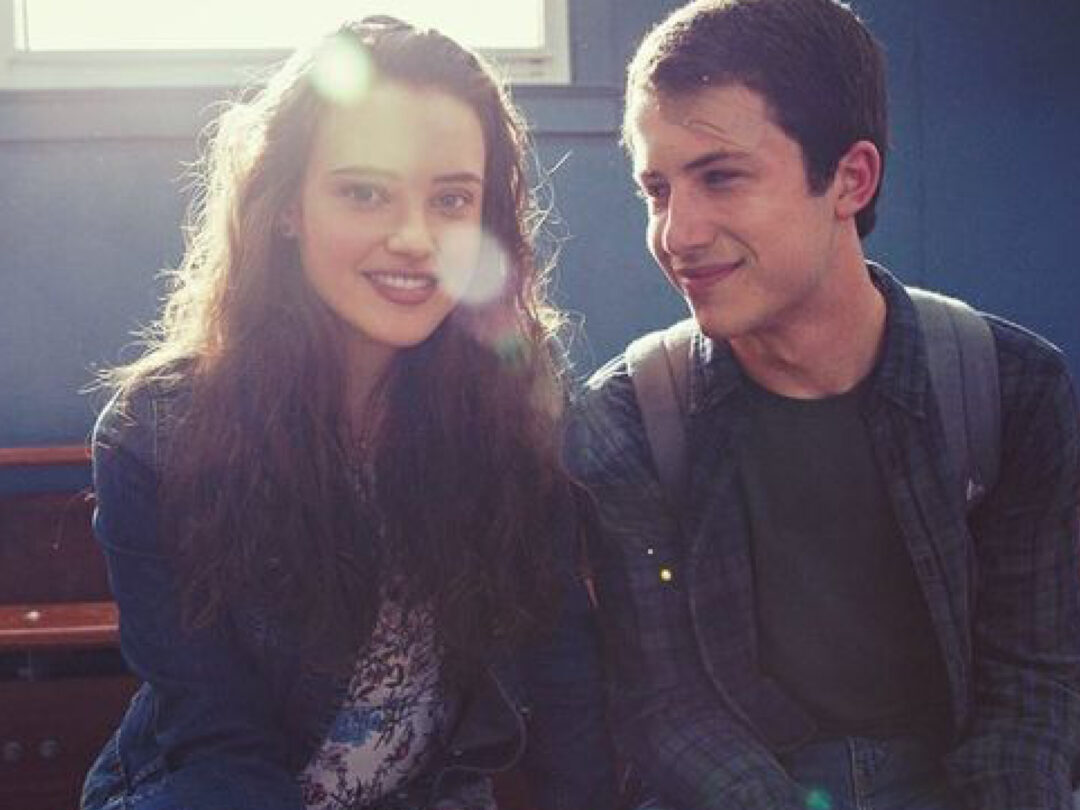 Auf dem Bild sieht man die beiden Hauptfiguren der Serie Hannah und Clay. Sie sitzen nebeneinander und lächeln sich an. Das Licht fällt durch ein Fenster hinter Hannah und lässt ihre Haare strahlen wie einen Heiligenschein.